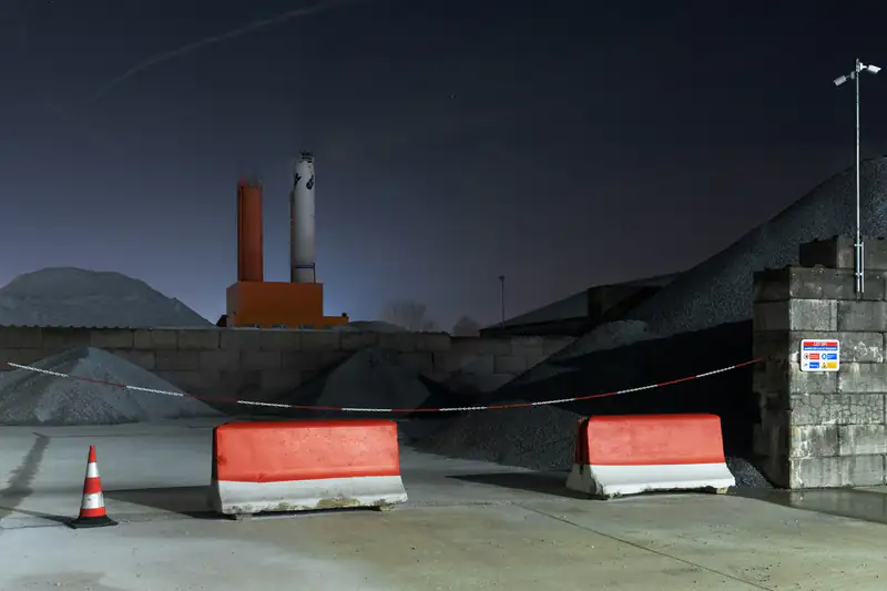 Fenced industrial yard at night with barriers and site lighting